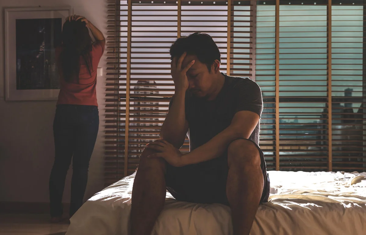 Husband and wife sitting head in hands on the bed in the dark bedroom with low light environment