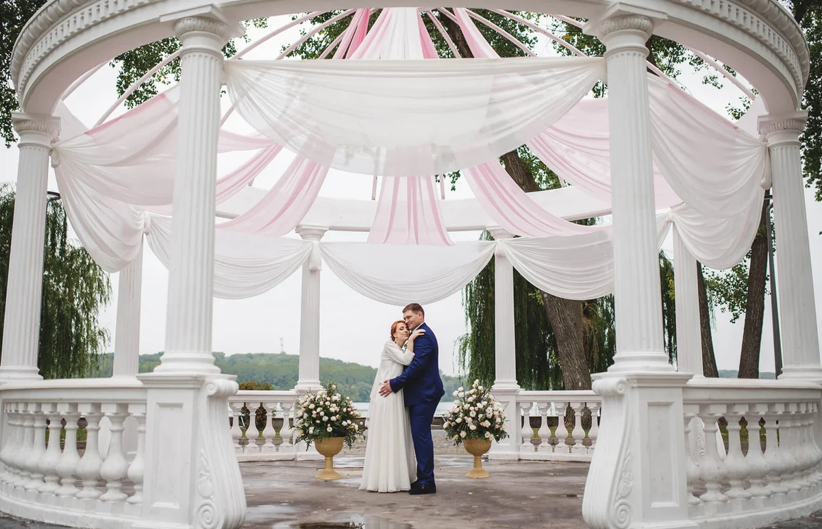 Wedding couple under large arch with pink material decoration with flowers