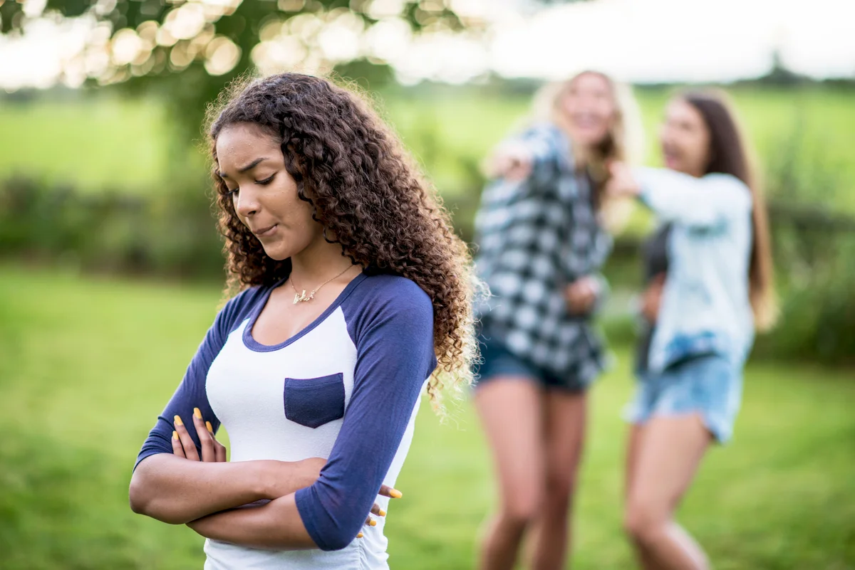 Two girls are laughing at another girl in the foreground. She looks very upset