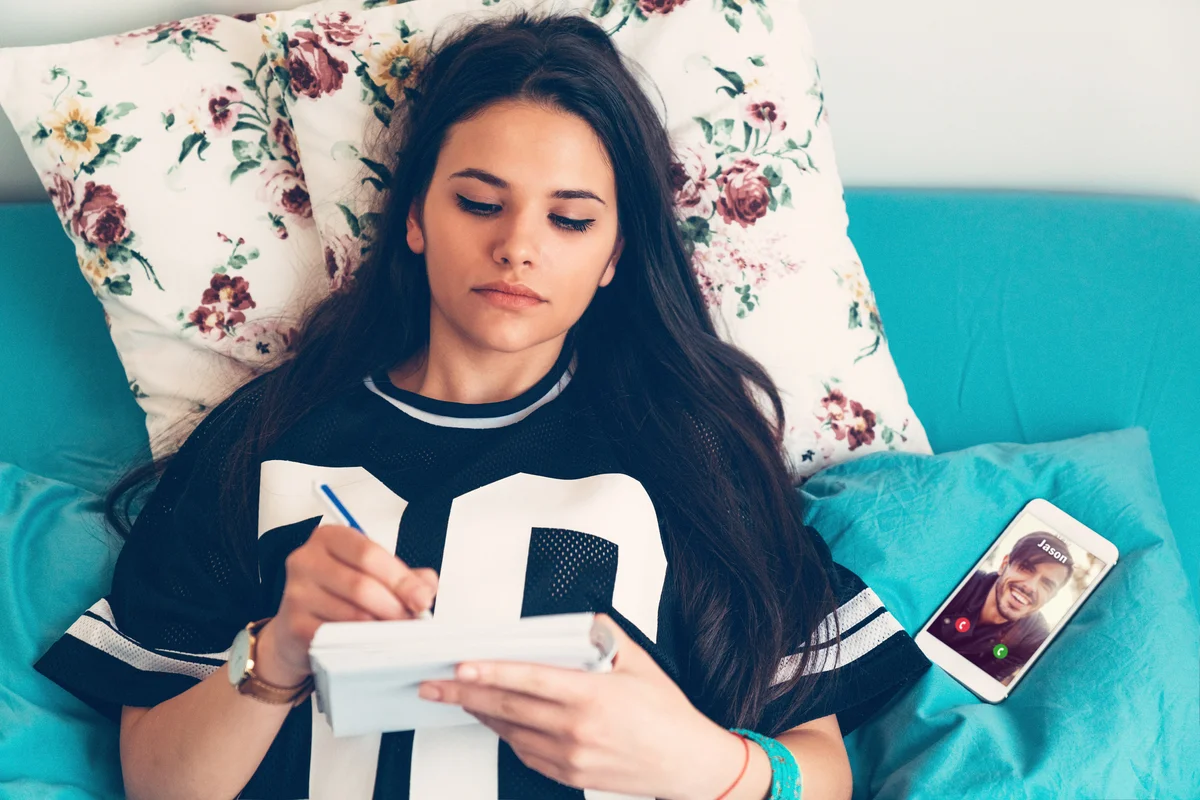 Teenage girl writing in her journal in bed