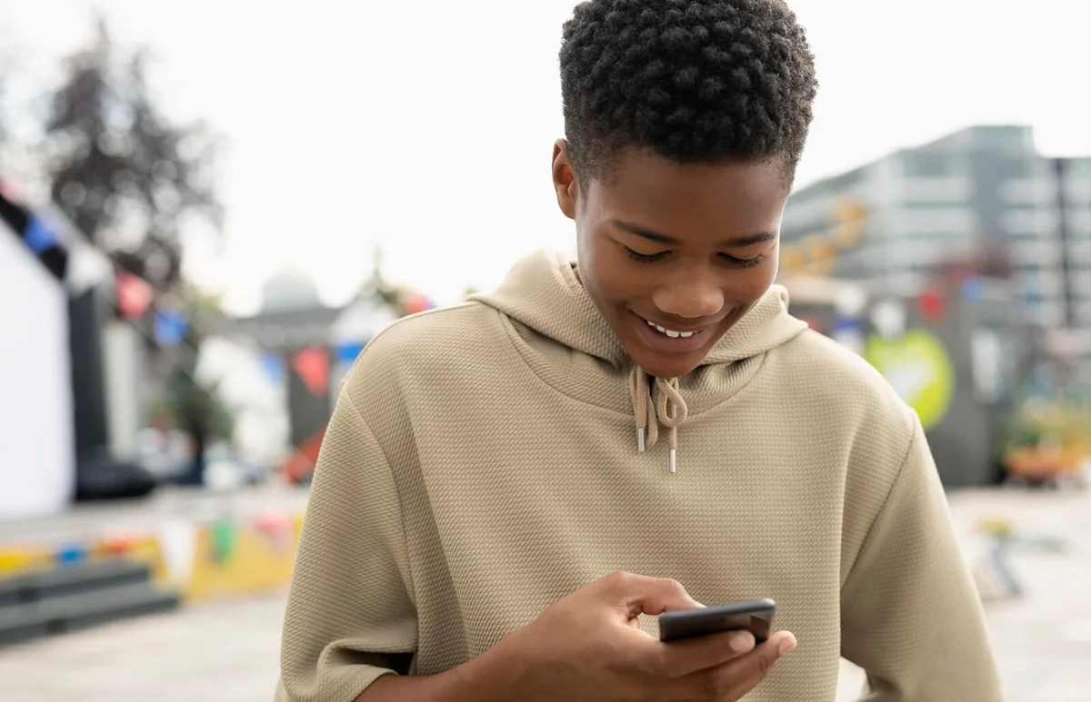 Smiling teenage boy texting with smart phone