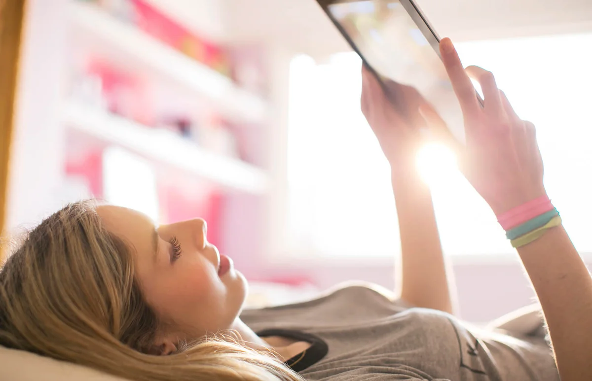 Teenage girl using digital tablet in sunny bedroom