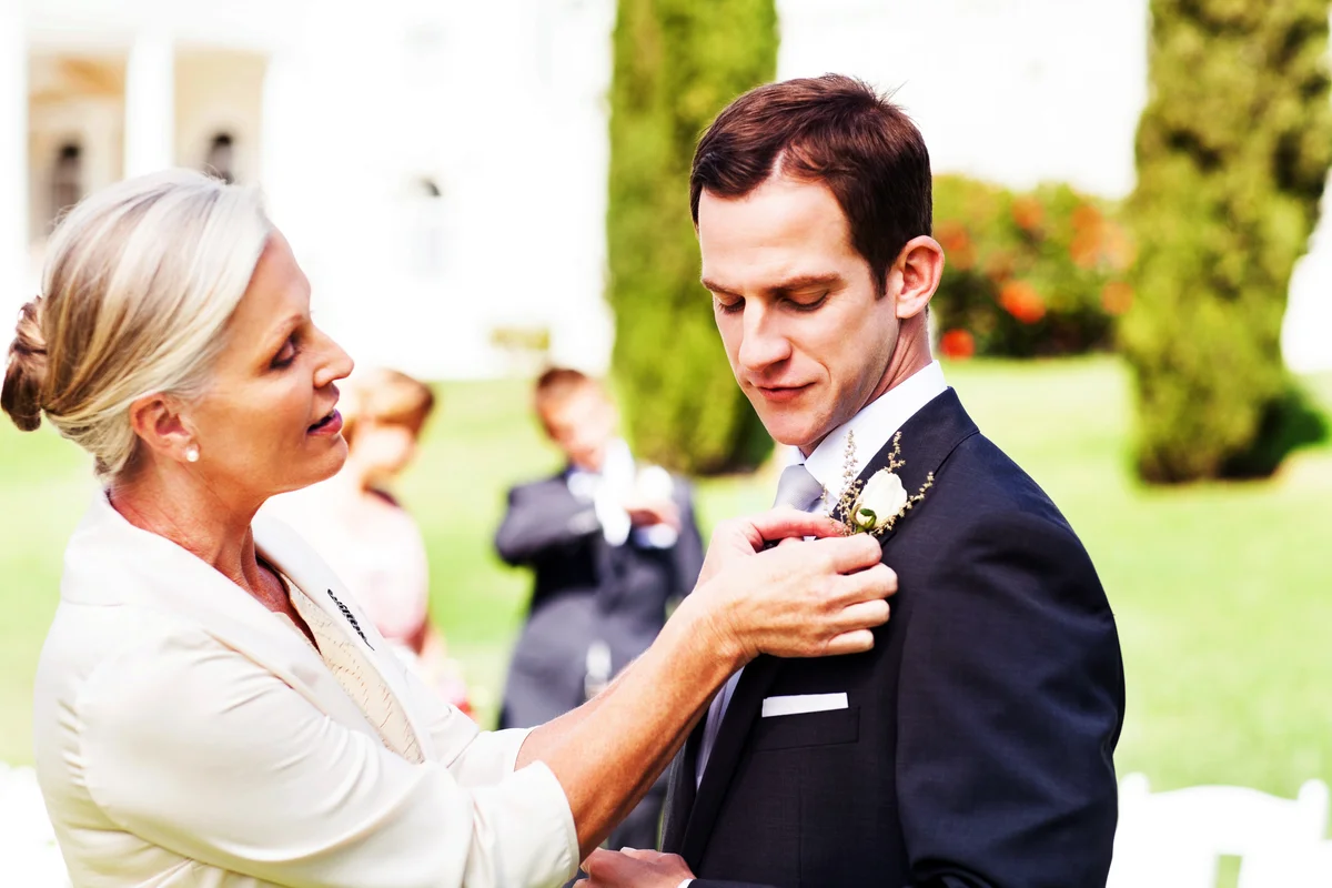 Mother Pinning Boutonniere On Groom's Suit At Garden Wedding