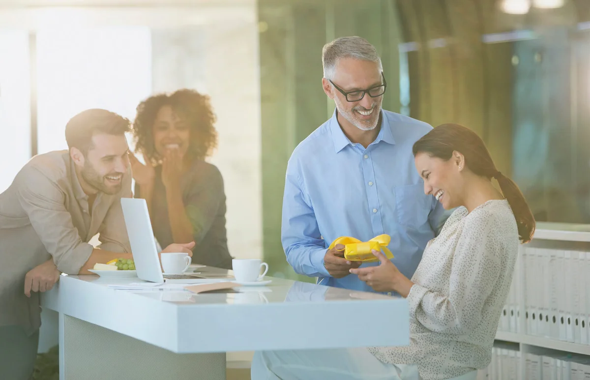 Businessman giving gift to pregnant businesswoman in office