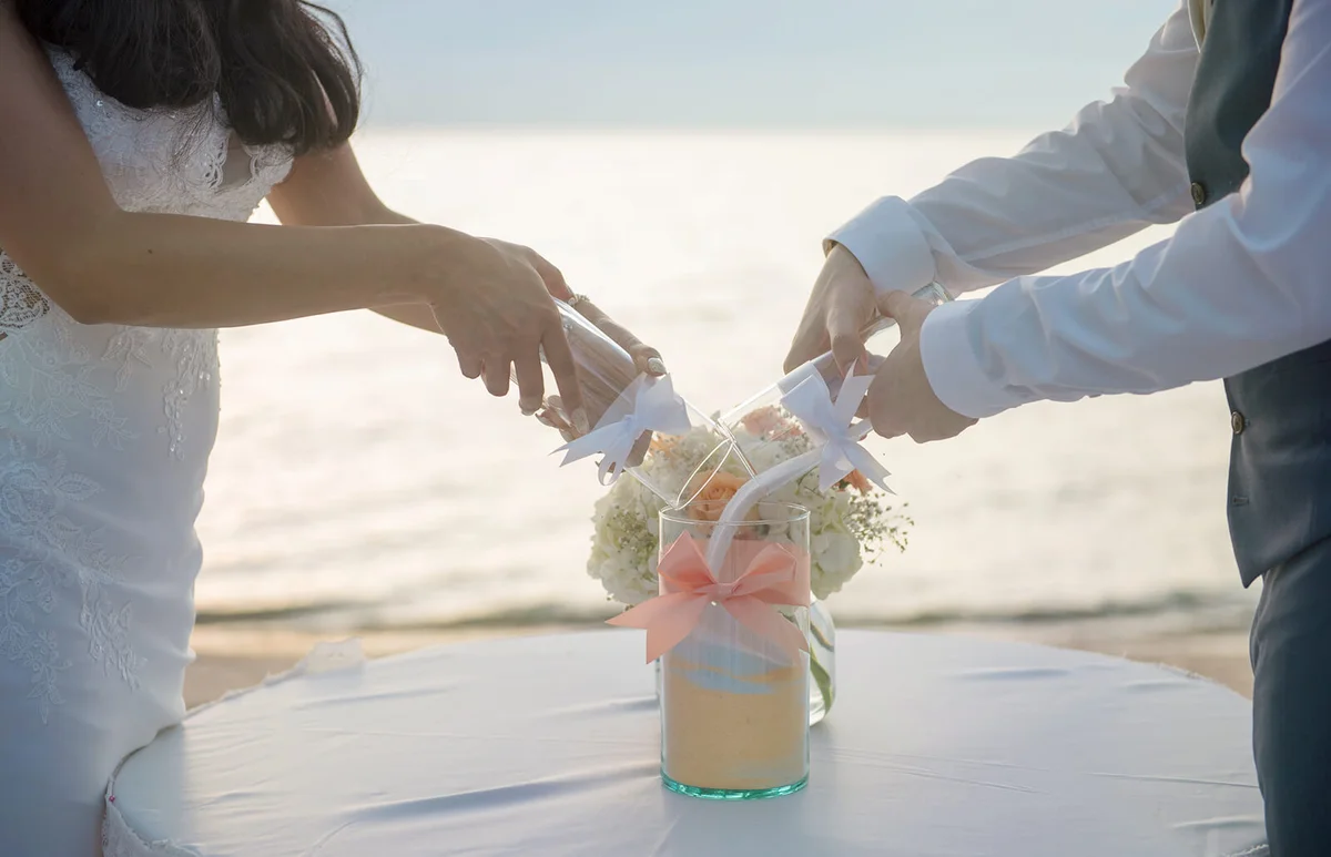 Wedding Couple Putting Sand In Container On Table At Beach