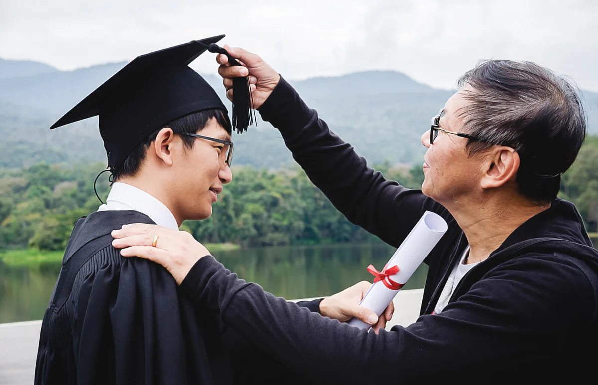 Father Adjusting Mortarboard Of Son Against Mountain