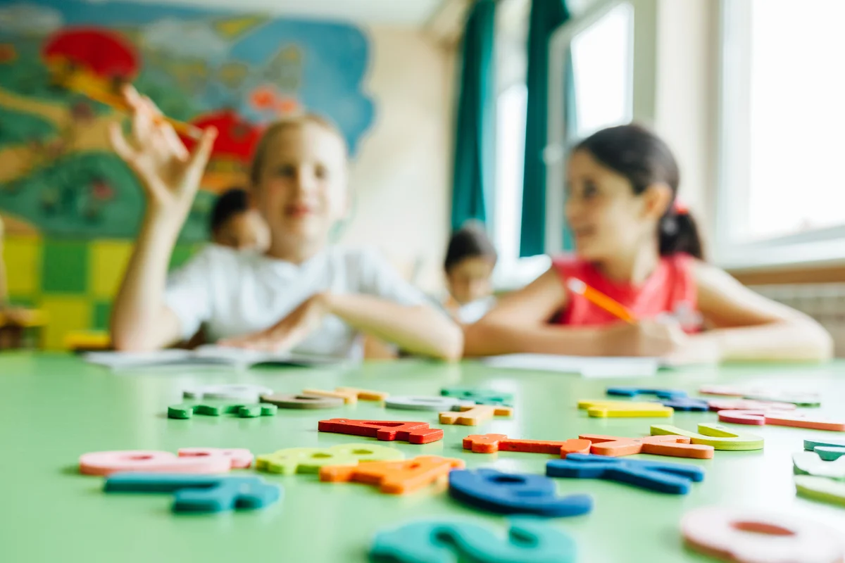 Kids with wooden toy plate alphabet in classroom