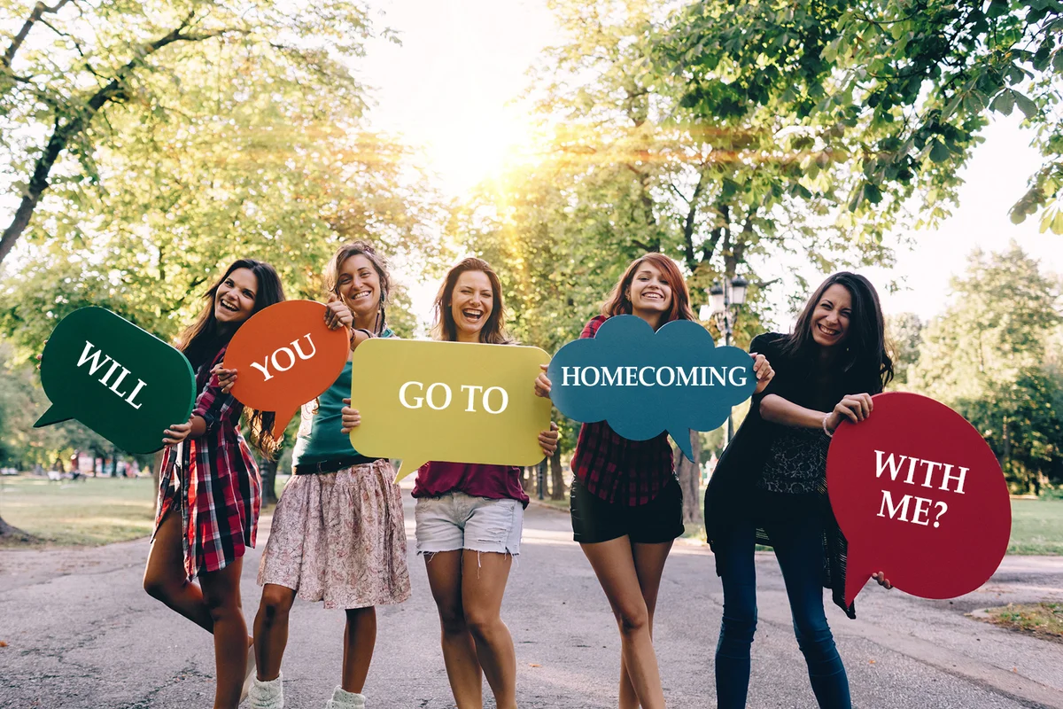Girls holding Will You Go To Homecoming With Me? signs