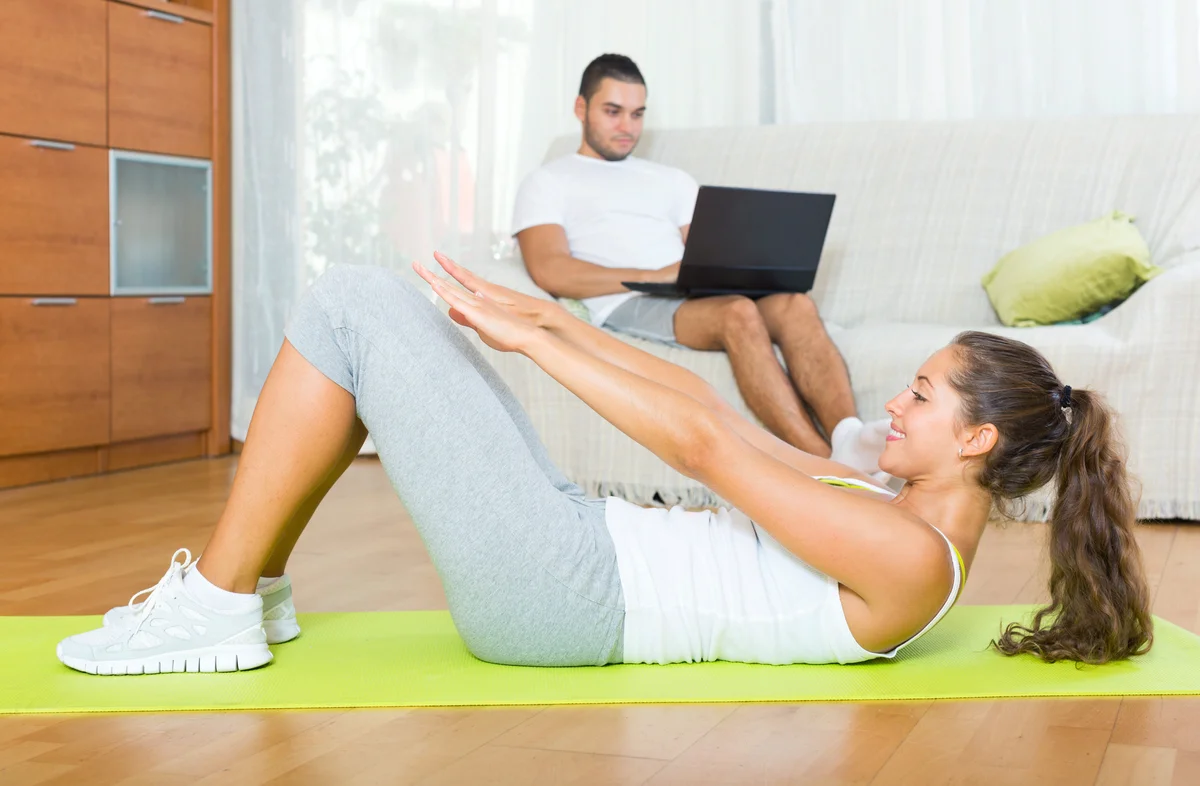 Girl practicing fitness and boyfriend resting on couch