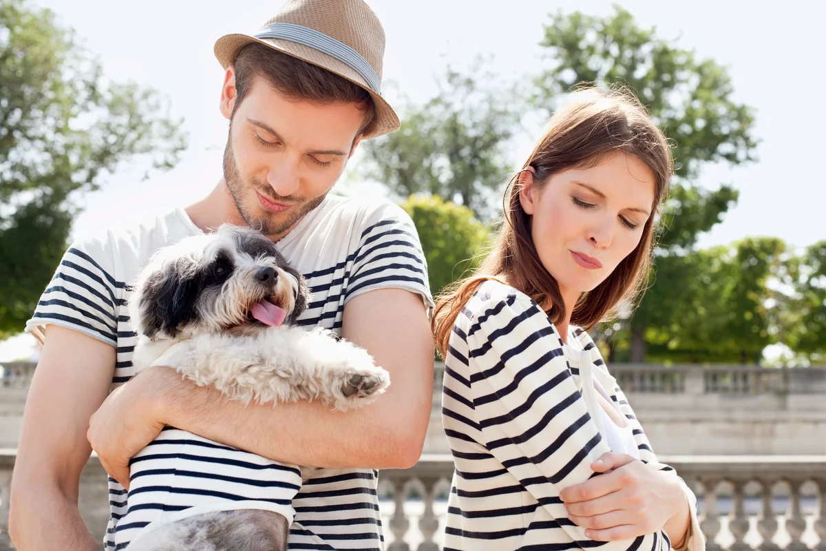 Man carrying a puppy and smiling with a woman looking upset