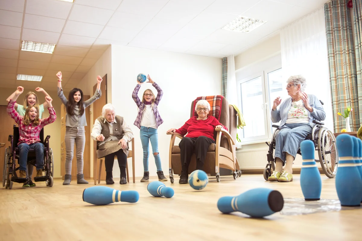 Girls playing bowling with senior women in rest home