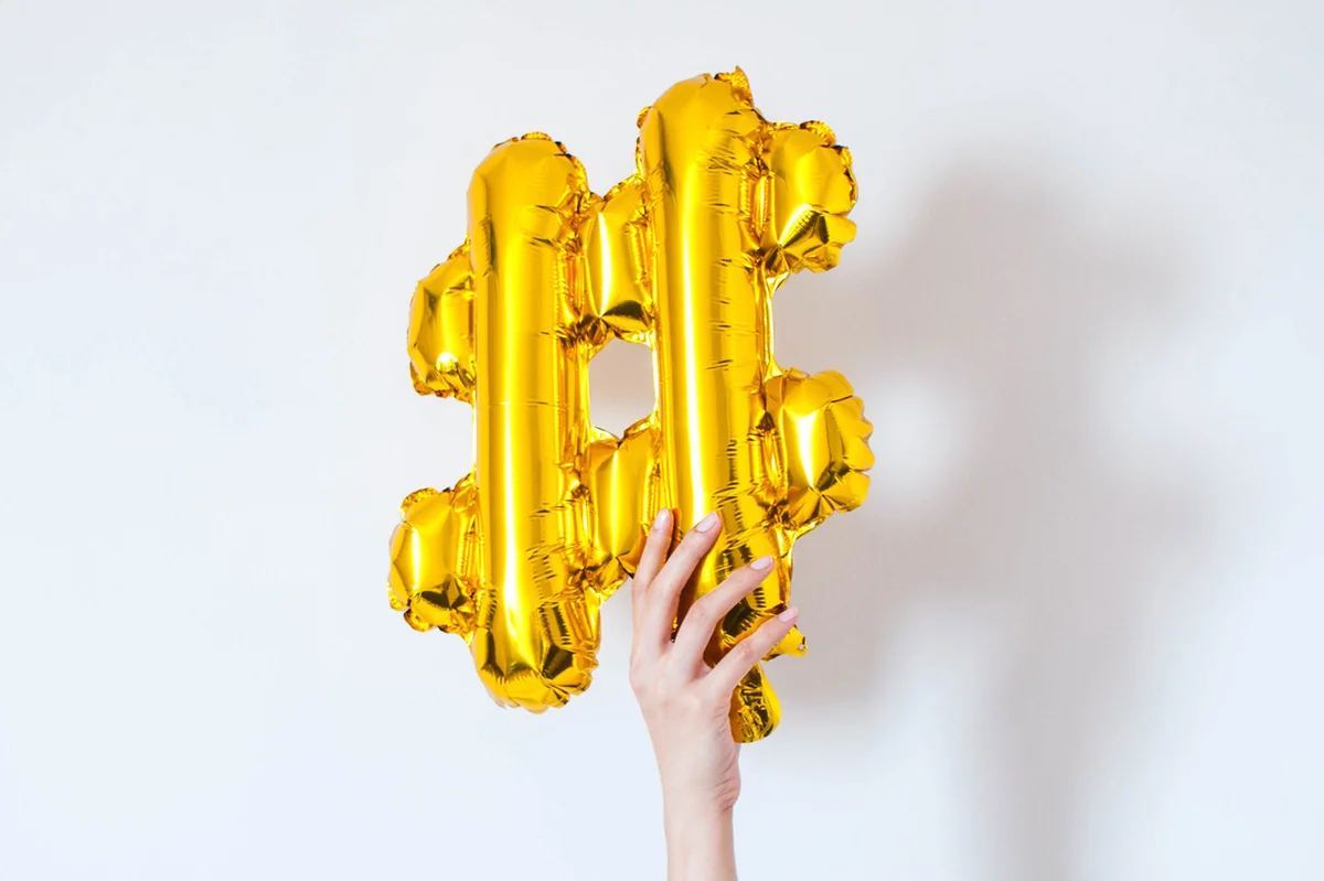 Hand holding a gold balloon hashtag symbol