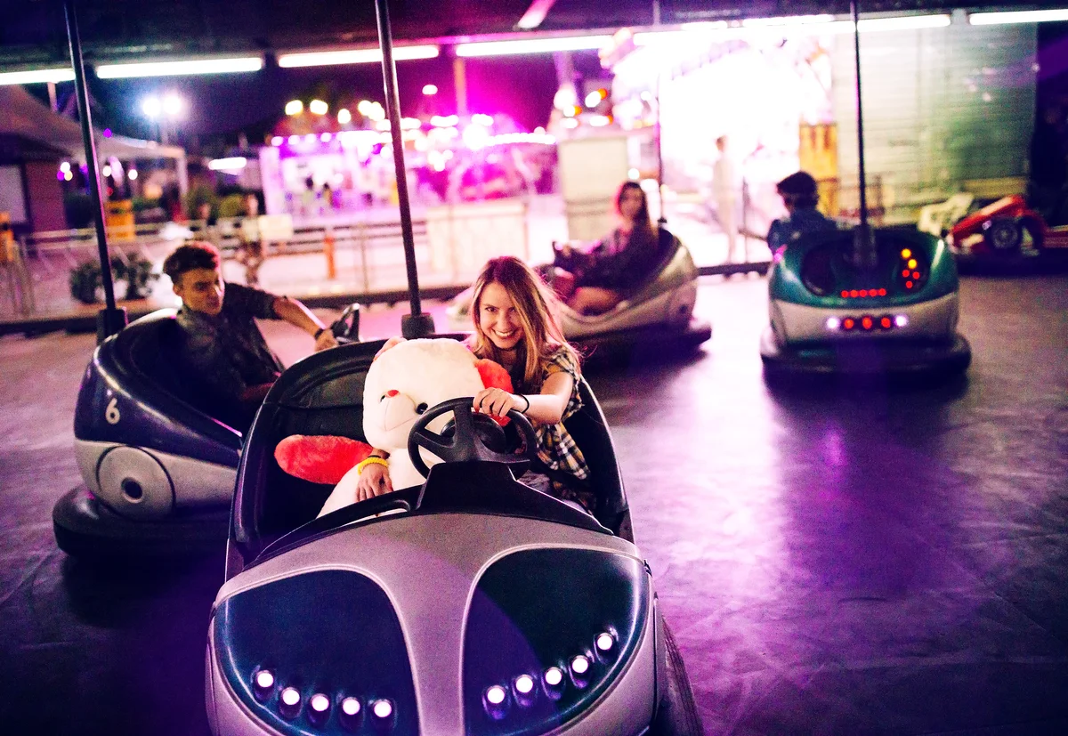 Teenage girl in bumper cars with teddy bear and friends