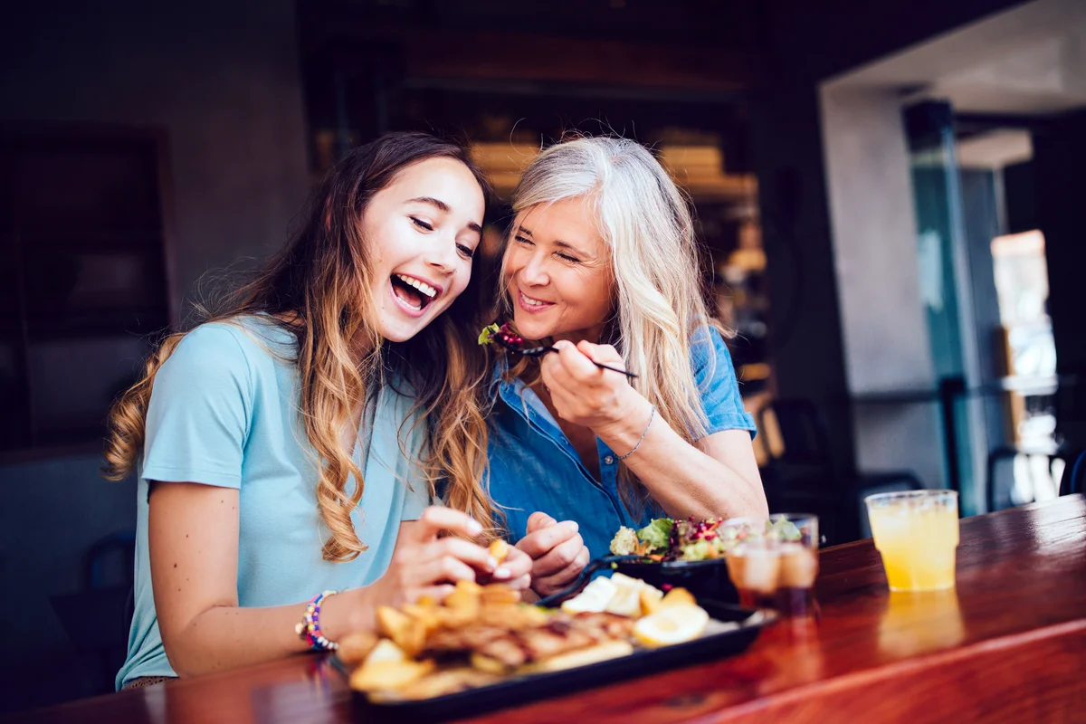 Smiling mother and teen daughter sharing lunch at a modern restaurant in the city