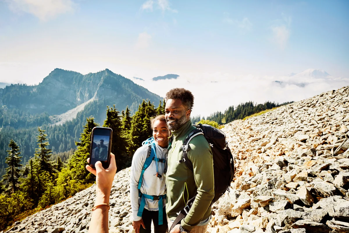 Woman taking photo of father and daughter with smart phone during hike in mountains