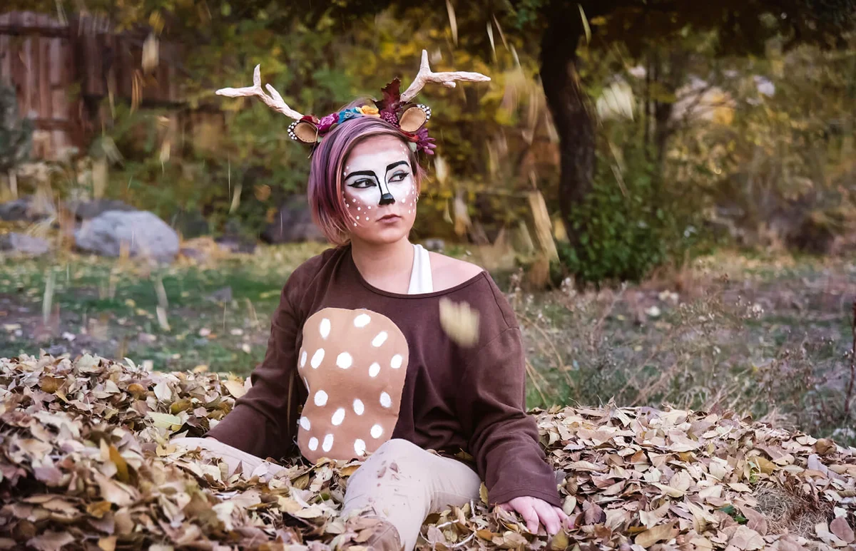 Girl sitting in a pile of leaves dressed as a deer