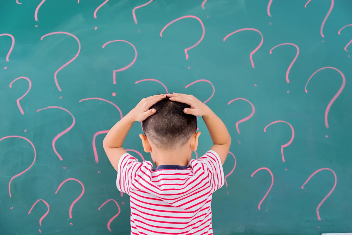 Asian little boy in front of blackboard with question marks