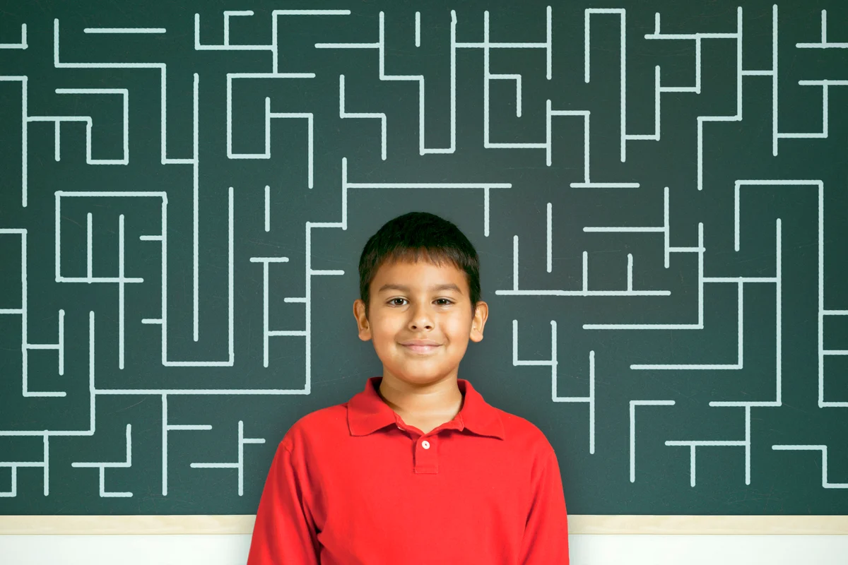 Child standing in front of a chalkboard with a maze on it