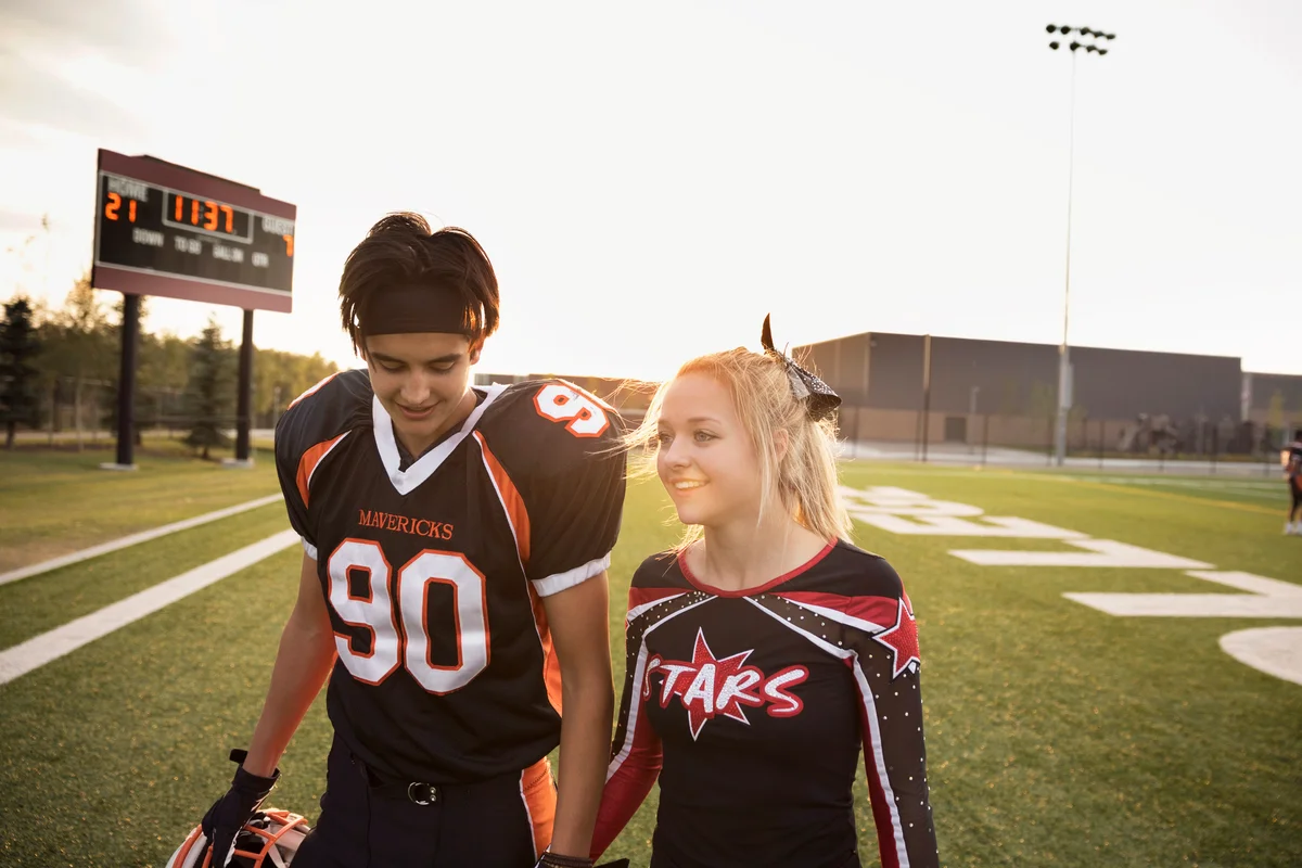 Teenage high school cheerleader and football player holding hands
