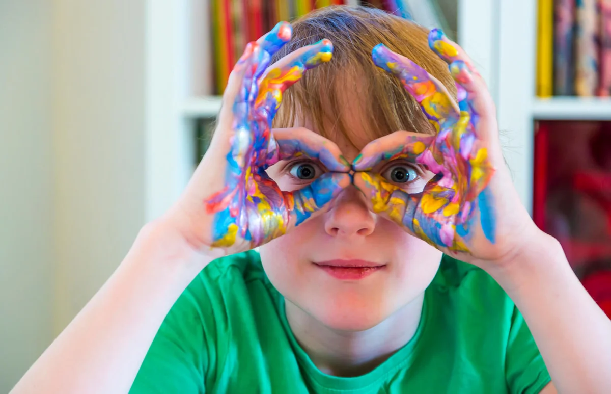 Boy looking through fingers, hands with finger paints