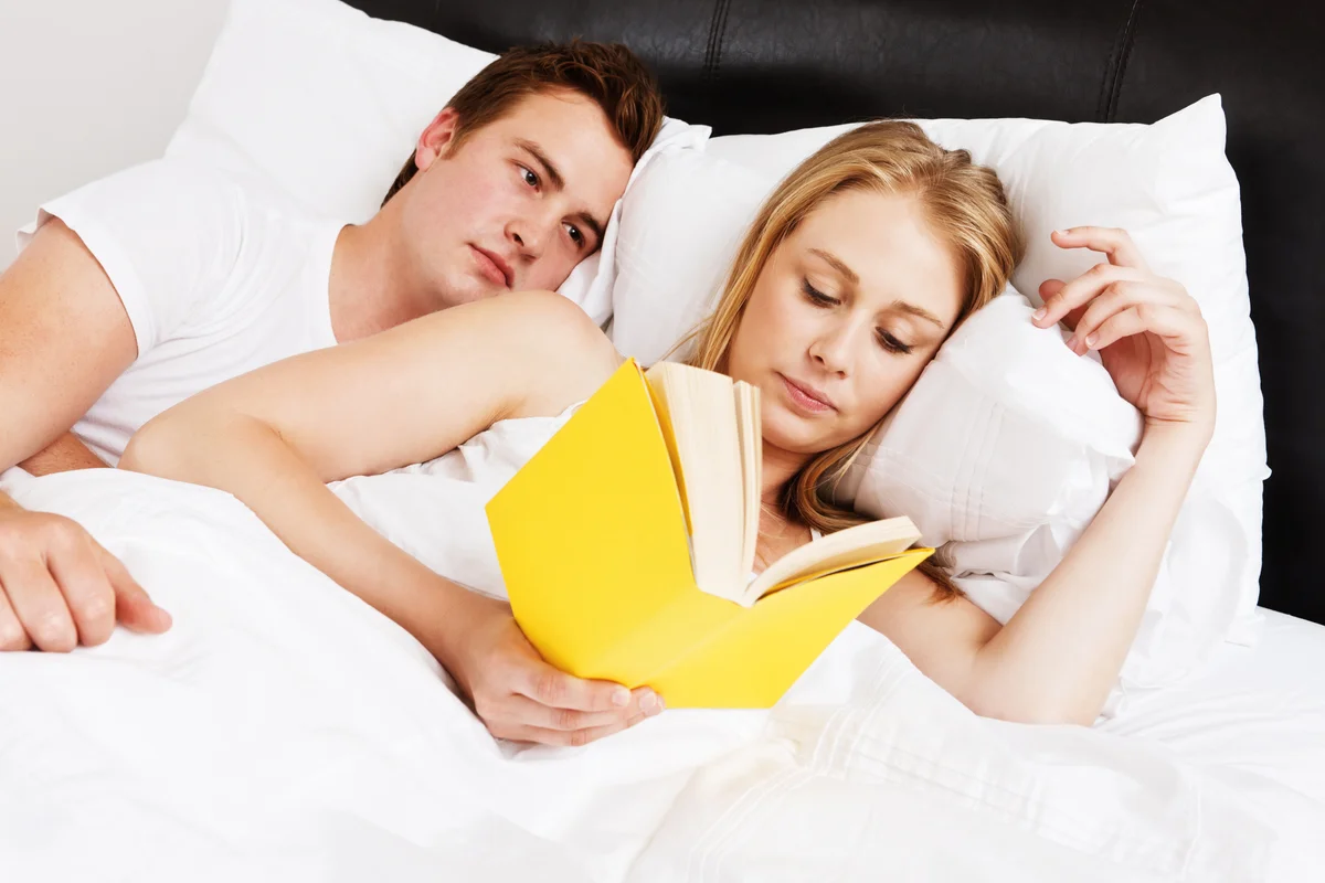 Woman reading in bed as man watches