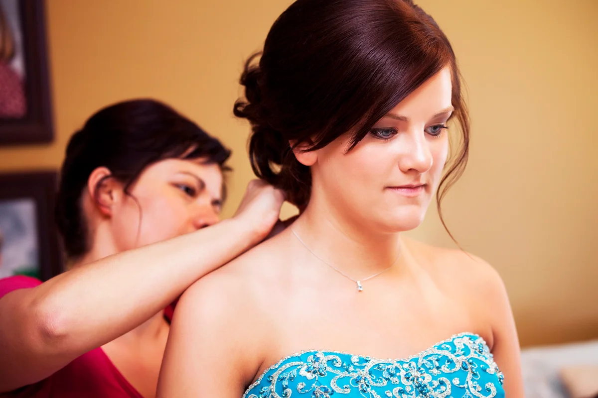 Young woman getting ready for her prom, her mother is putting on her necklace