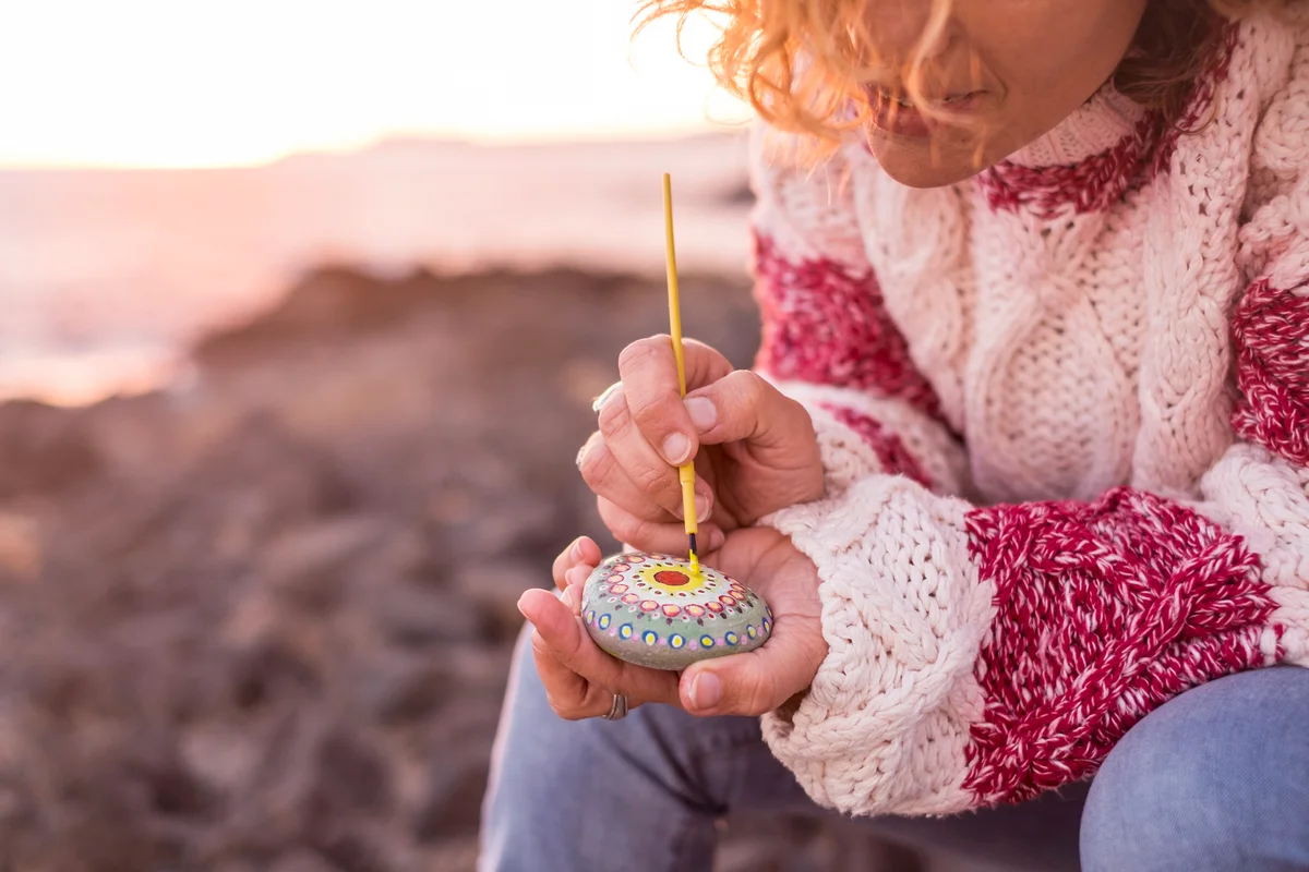 Woman Painting Pebble At Beach During Sunset