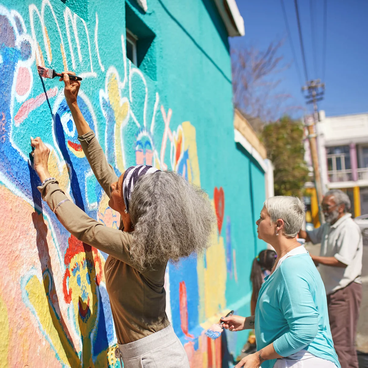Senior community volunteers painting vibrant mural on sunny urban wall