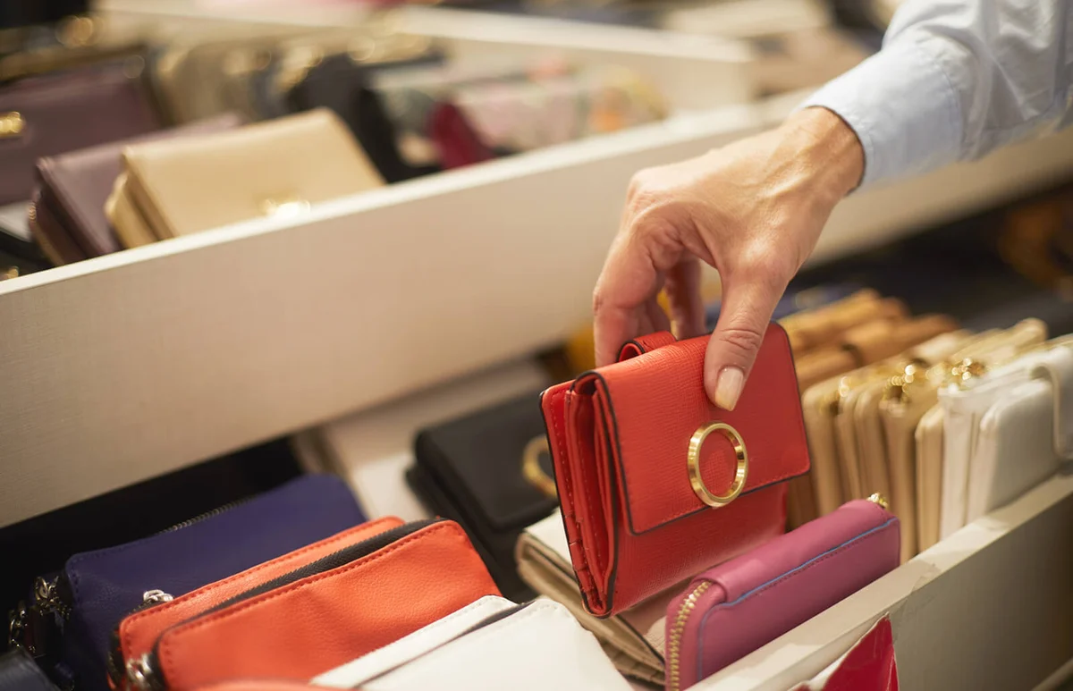 woman picking up a red wallet from a rack