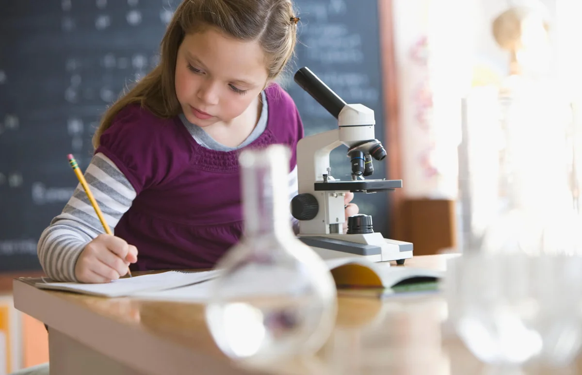 Caucasian girl looking into classroom microscope