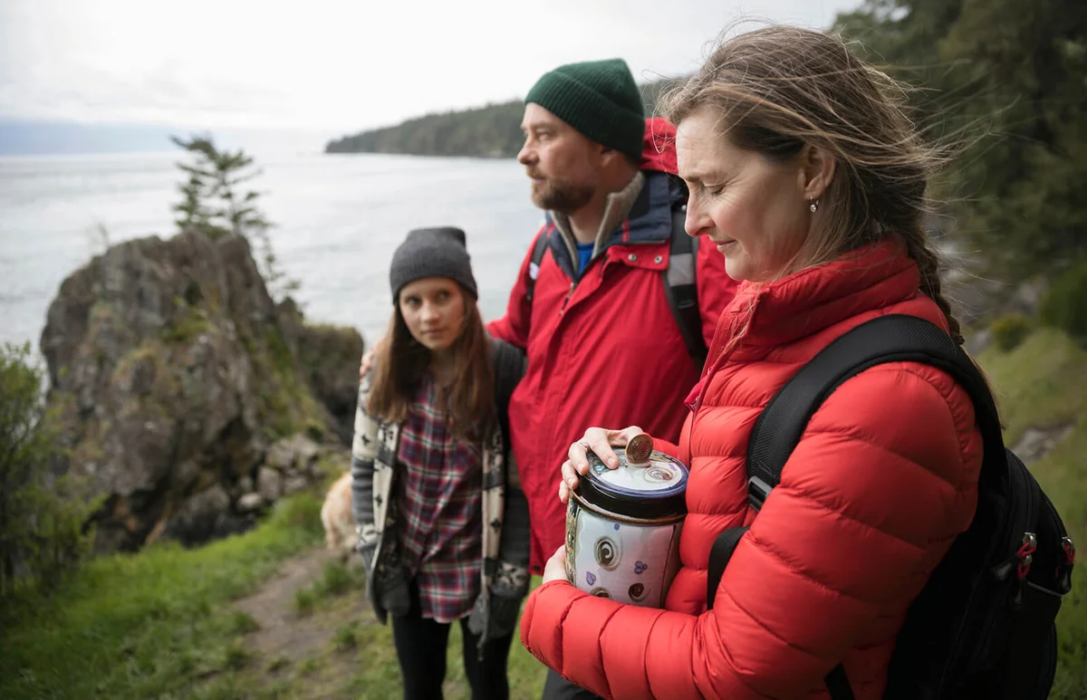 Family with urn spreading ashes on cliff overlooking ocean