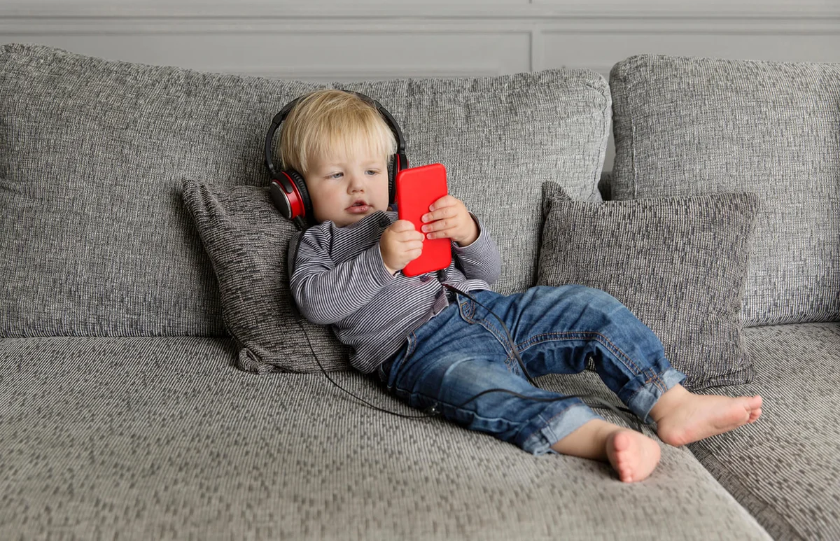 Toddler lying on couch listening music with headphones