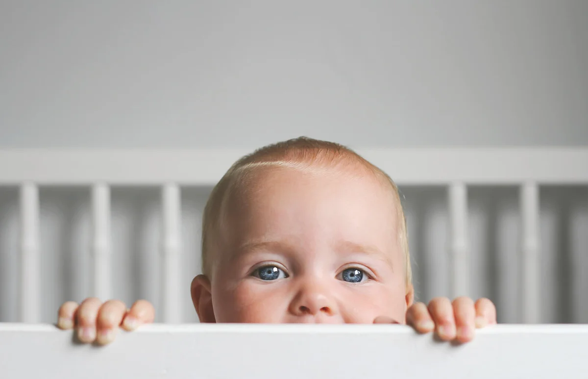 baby peeking over the bars of her crib.