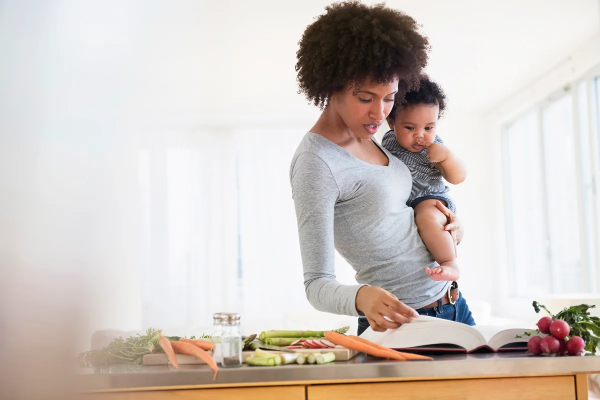 Mother reading cookbook while holding baby son