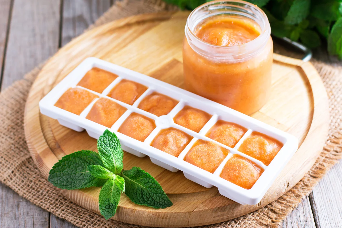 Ice tray with fresh vegetable puree on wooden background