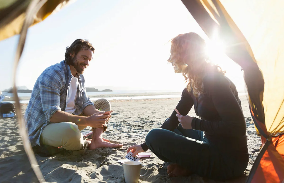 Couple camping playing cards on beach at sunset