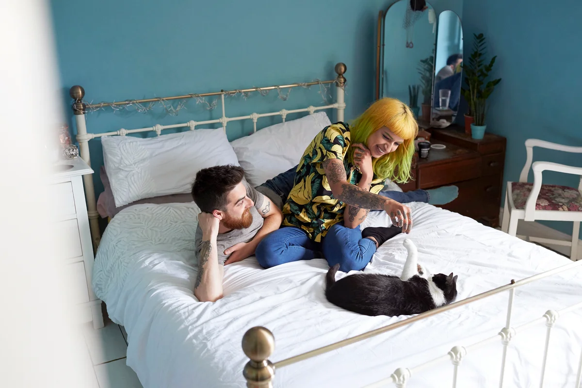 Young hipster couple lying on their bed together playing with their pet cat