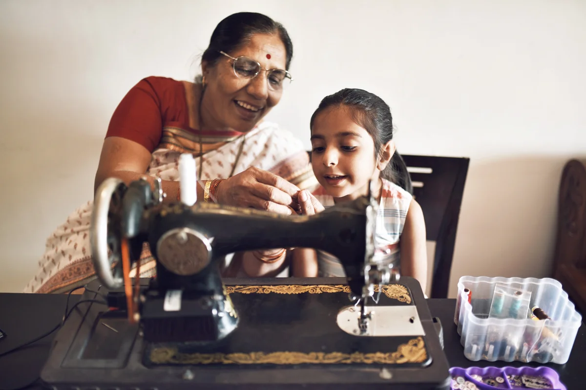 Senior woman working on sewing machine along with granddaughter