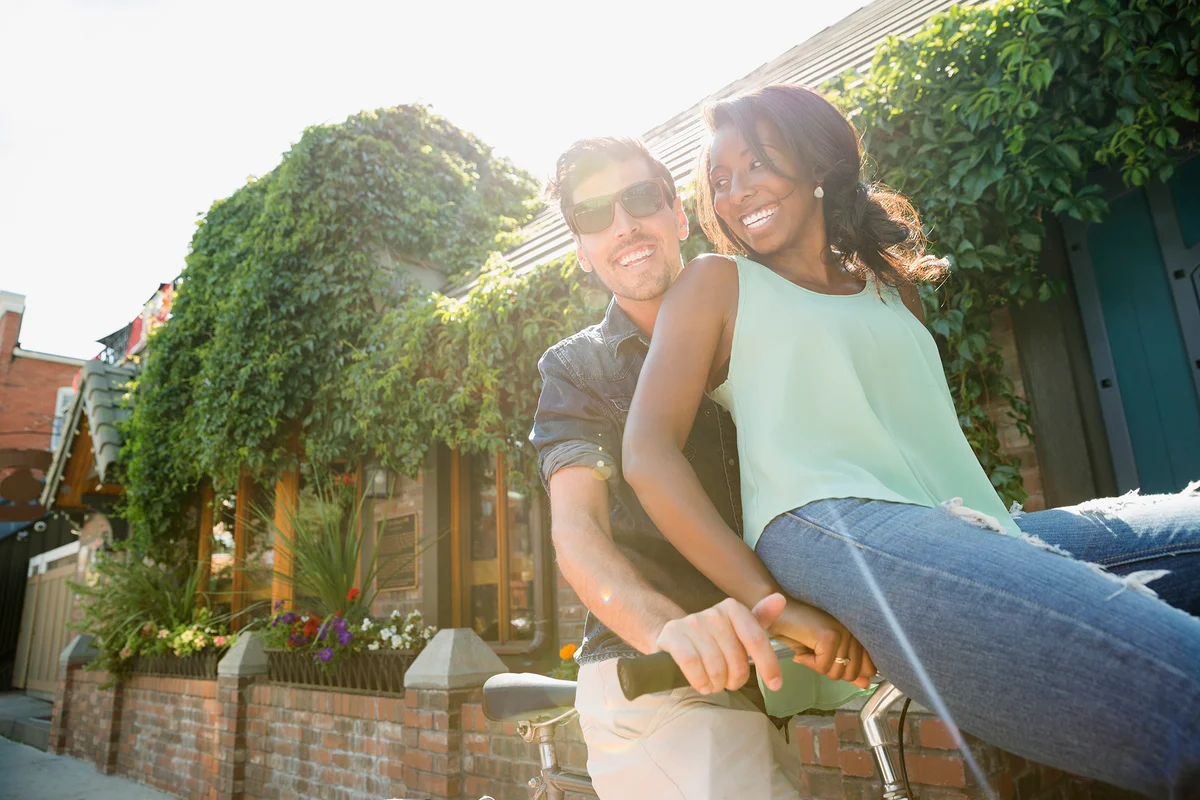 Playful couple riding bicycle on sunny sidewalk