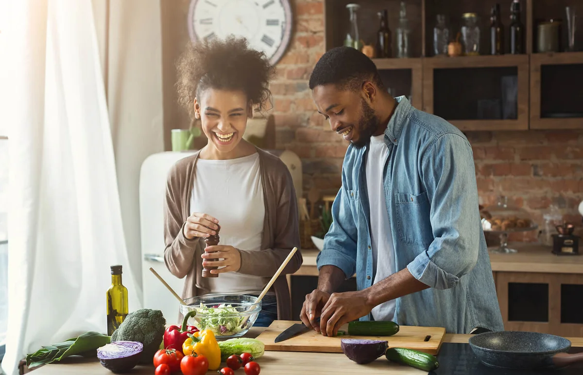 Laughing couple preparing salad in kitchen