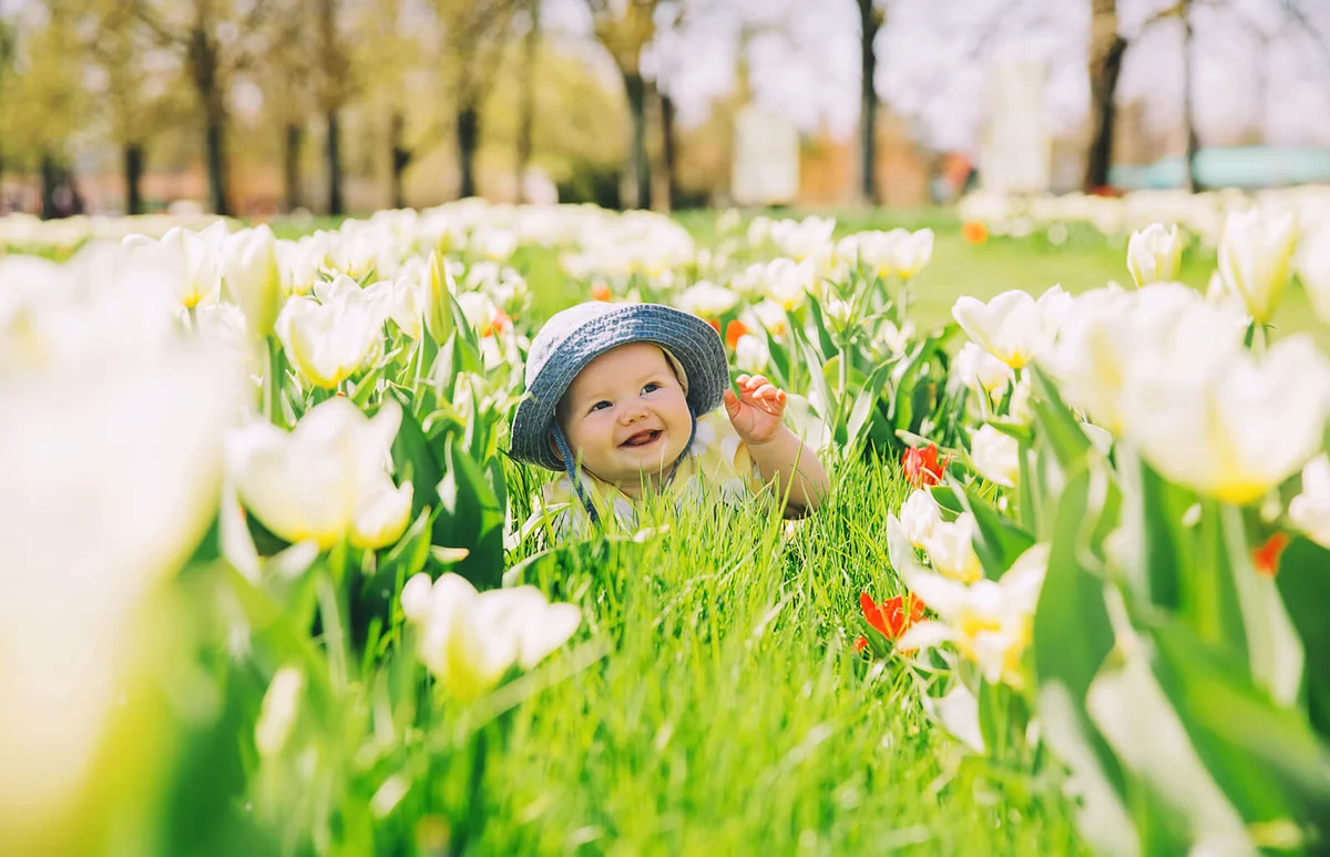 Happy smiling baby girl lying on blanket in green grass of tulips field