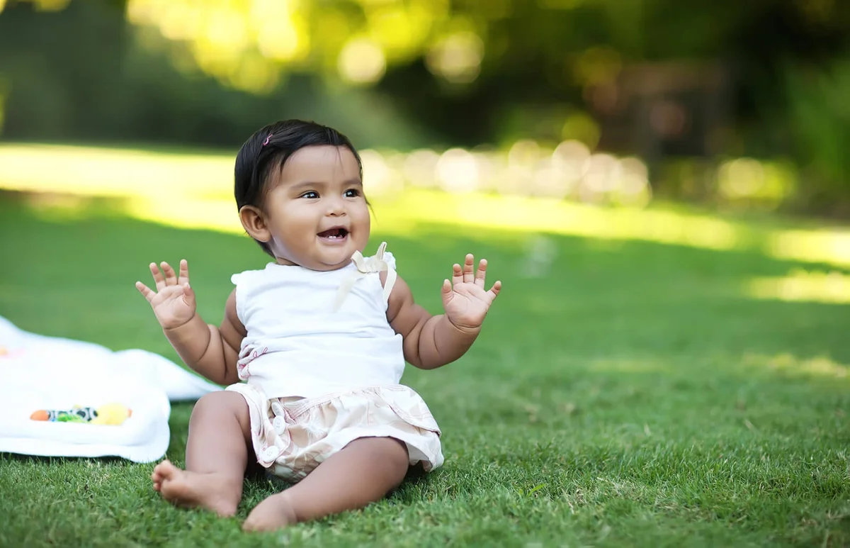 Happy baby girl sitting in the grass by herself