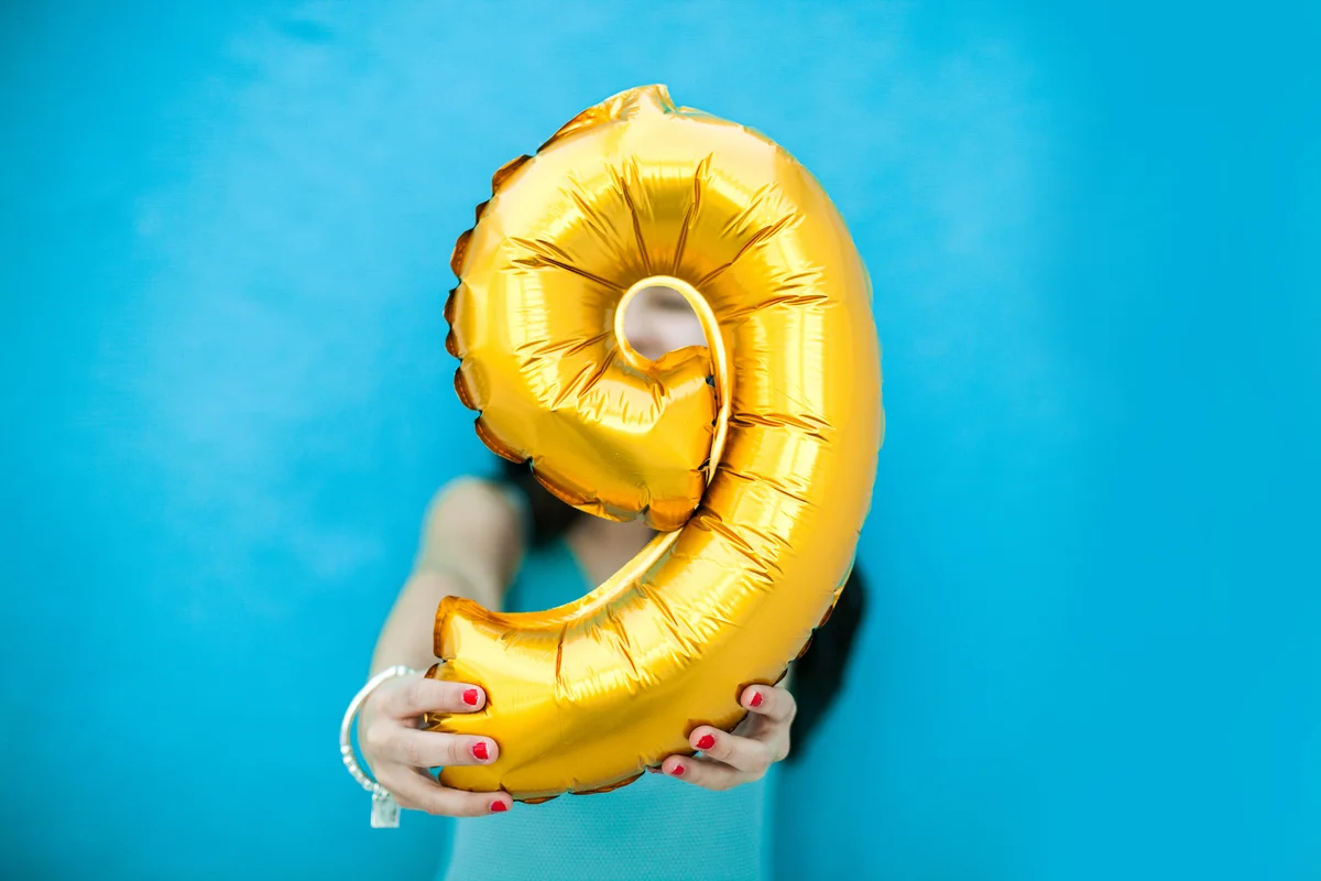 Brunette girl in blue dress holding a number 9 balloon