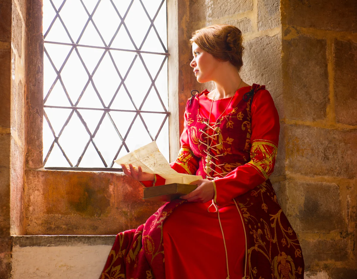 Woman in medieval costume reading at castle window
