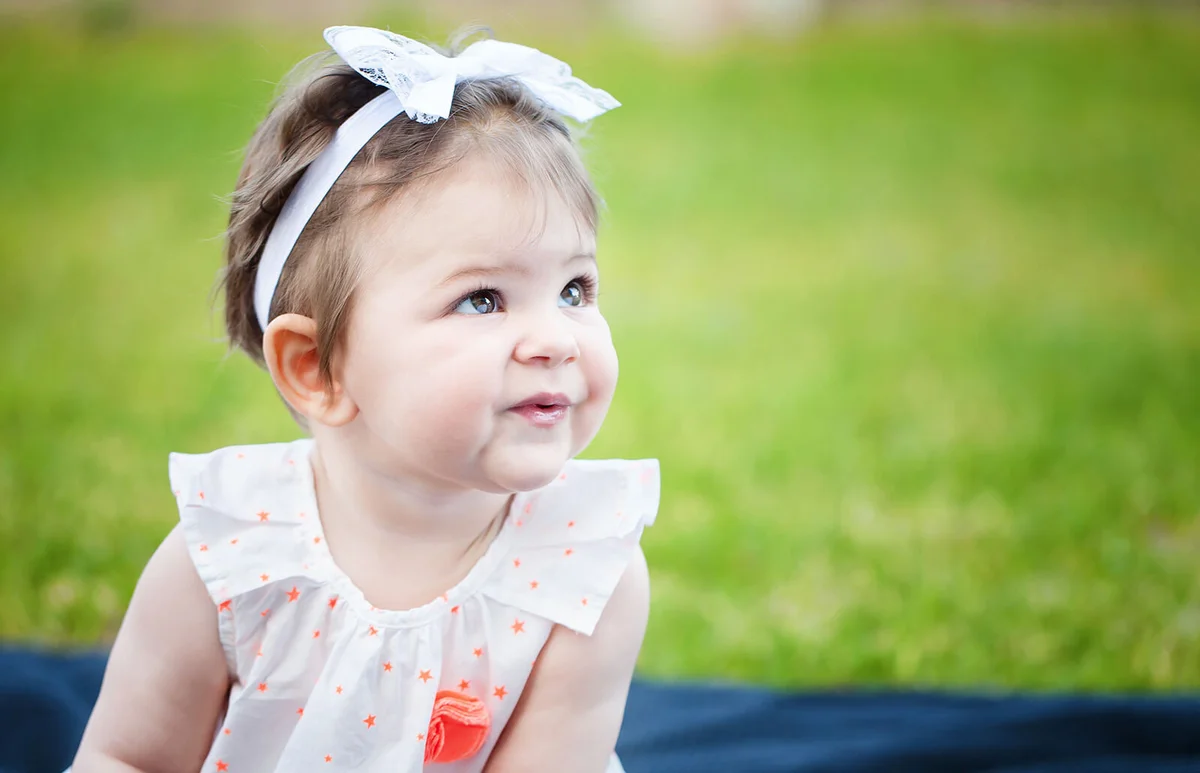 Cute baby girl sitting on the grass looking away