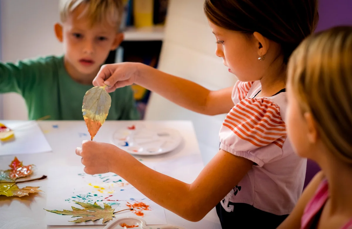 Children dipping fall leaves in paint