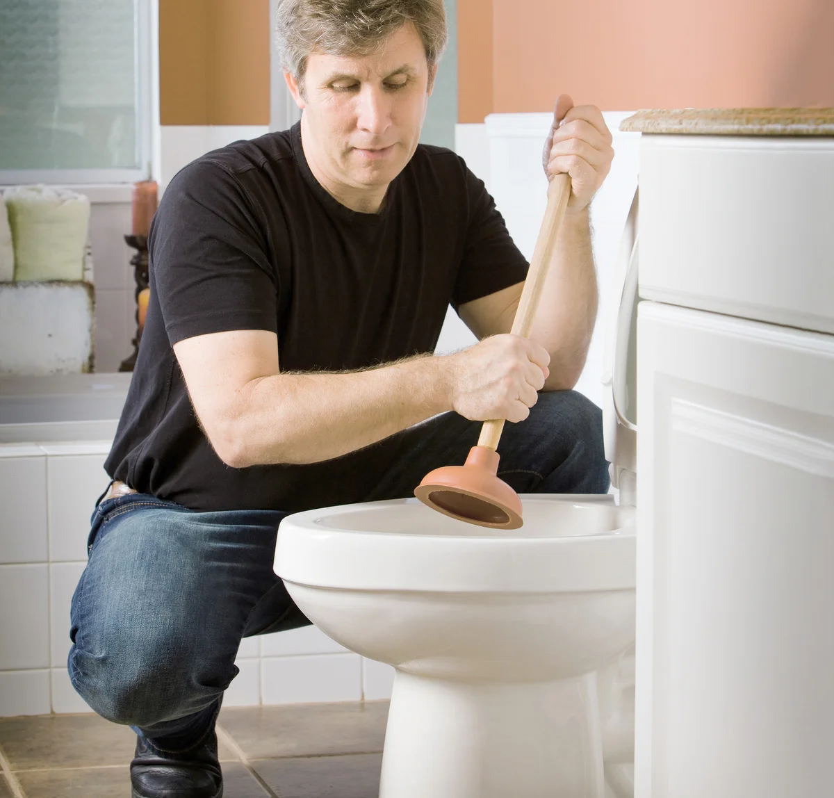 A man uses a plunger to unplug a home toilet