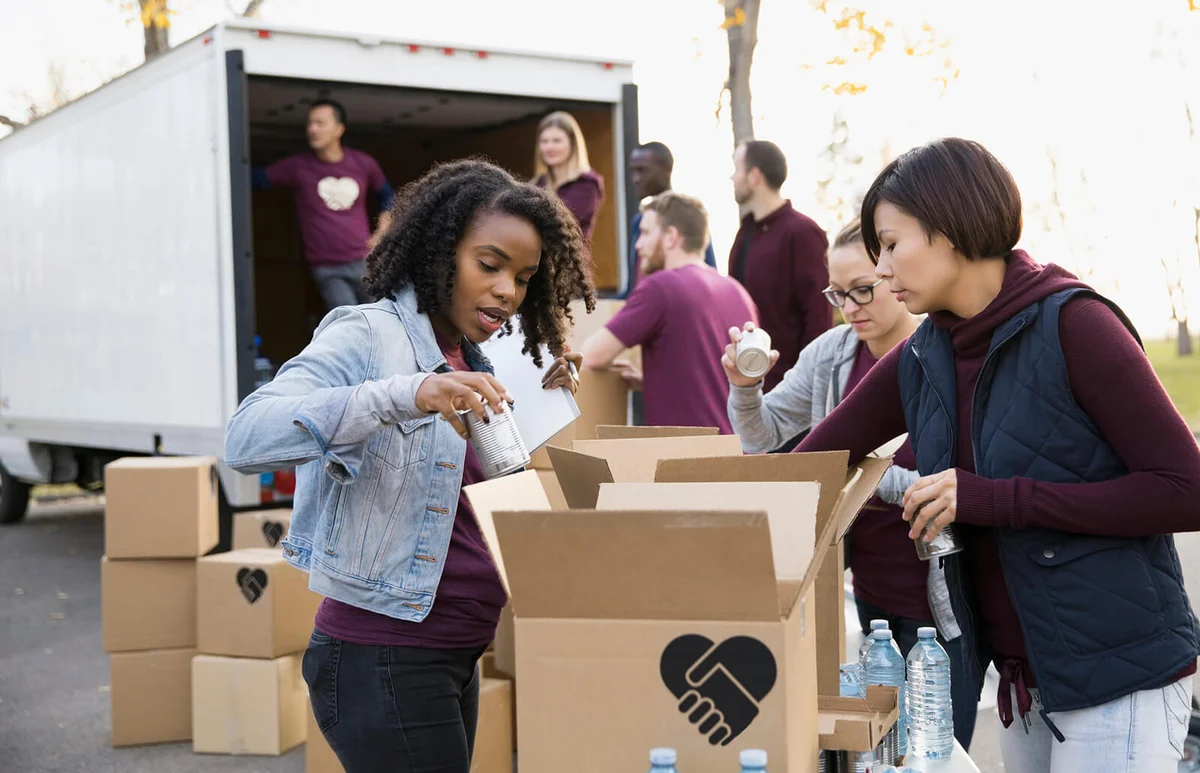 Volunteers packing food and water into cardboard boxes outside truck