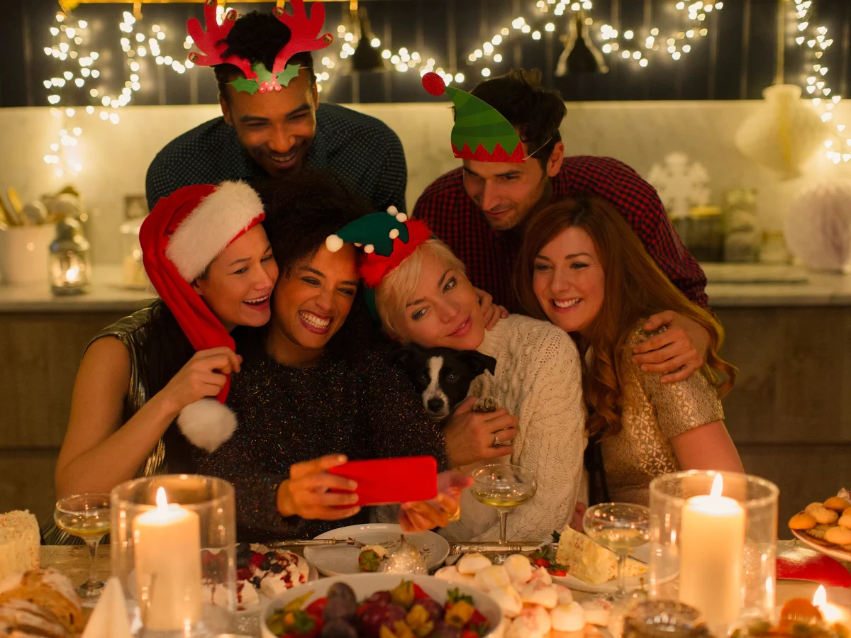 Playful friends with dog taking selfie at candlelight Christmas table