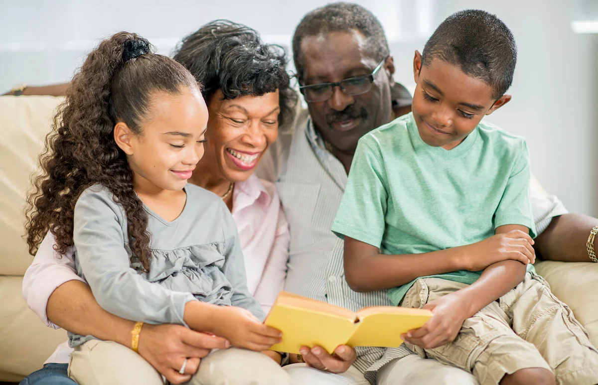 grandmother and grandfather are reading a book to their children while sitting on the couch together